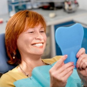Older dental patient admriing her smile in mirror