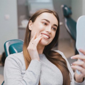 Young woman in dental chair looking at her smile in mirror